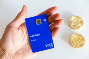 CoinbaseCard (Visa Debit) in a Hand with Bitcoin in background